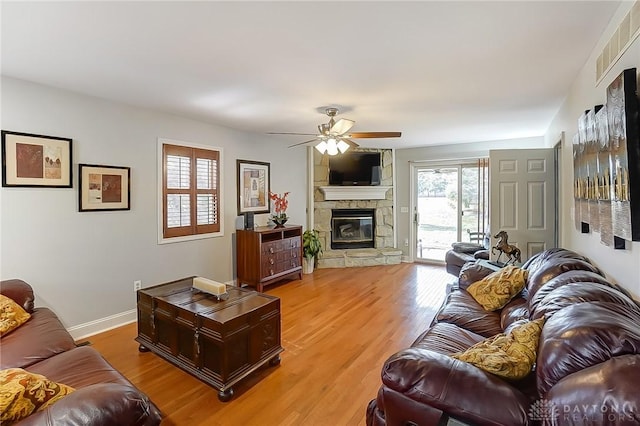 living room with light wood finished floors, visible vents, baseboards, ceiling fan, and a stone fireplace