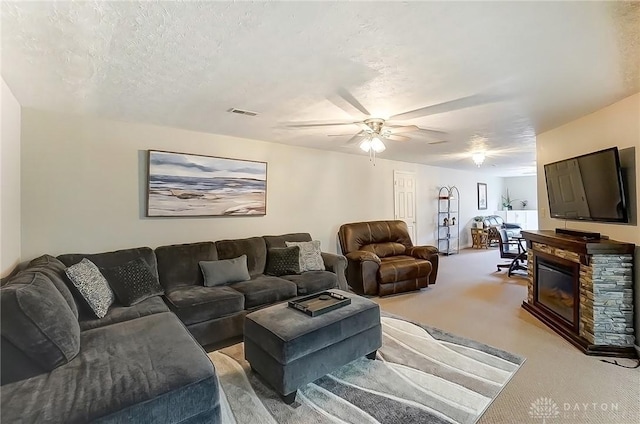 living area with a fireplace, visible vents, light carpet, ceiling fan, and a textured ceiling