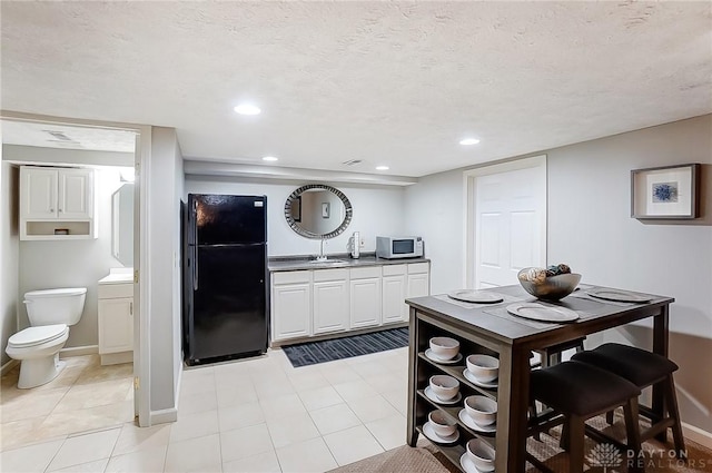 kitchen with baseboards, white microwave, freestanding refrigerator, a textured ceiling, and a sink