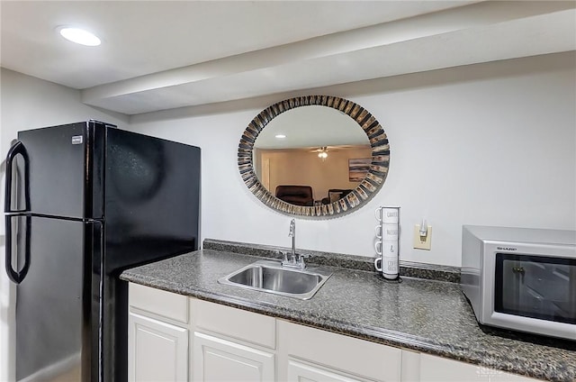 kitchen with white cabinets, dark countertops, white microwave, freestanding refrigerator, and a sink