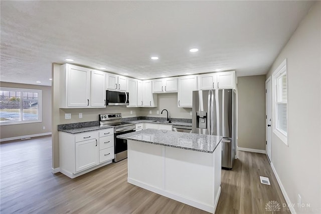 kitchen with a sink, stone counters, light wood-style floors, and appliances with stainless steel finishes