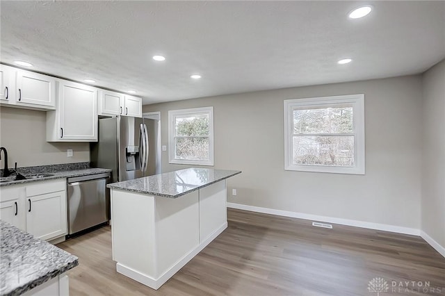 kitchen with a sink, a center island, stainless steel appliances, white cabinets, and light wood finished floors