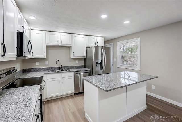 kitchen with a center island, light wood-style flooring, appliances with stainless steel finishes, white cabinets, and a sink