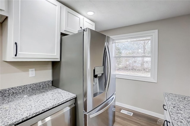 kitchen featuring visible vents, baseboards, stainless steel refrigerator with ice dispenser, wood finished floors, and white cabinetry