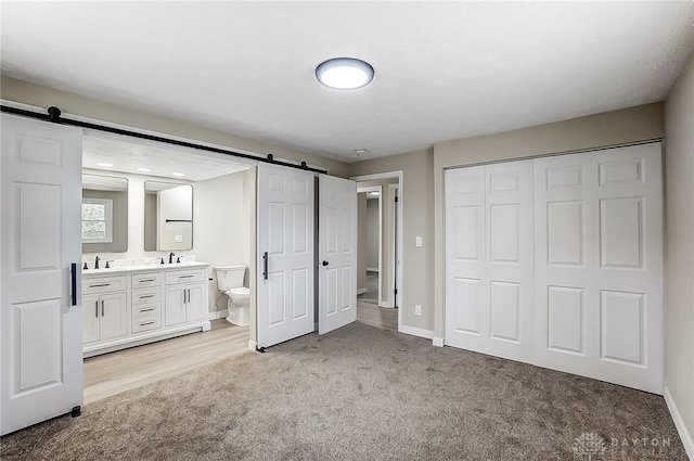 unfurnished bedroom with light carpet, a closet, a barn door, and a sink