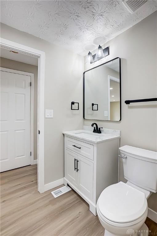 half bathroom featuring visible vents, toilet, wood finished floors, and vanity