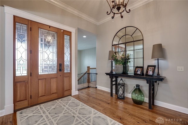 foyer entrance with a notable chandelier, ornamental molding, wood finished floors, plenty of natural light, and baseboards