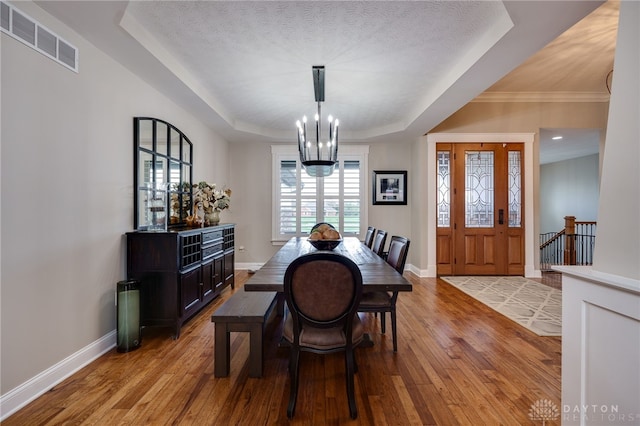 dining area featuring a tray ceiling, light wood-type flooring, visible vents, and baseboards