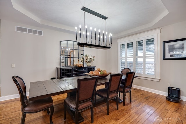 dining room with a tray ceiling, baseboards, visible vents, and hardwood / wood-style floors