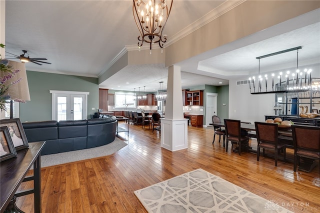 living room featuring visible vents, crown molding, light wood finished floors, and ceiling fan with notable chandelier