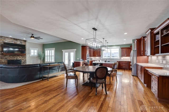 dining area with light wood finished floors, french doors, crown molding, a stone fireplace, and recessed lighting