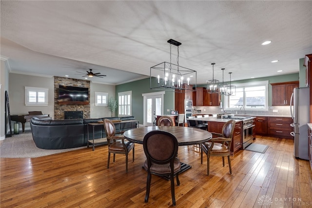 dining room featuring light wood-style floors, crown molding, a stone fireplace, and ceiling fan