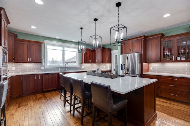 kitchen with light wood finished floors, a kitchen island, a breakfast bar area, stainless steel appliances, and a sink