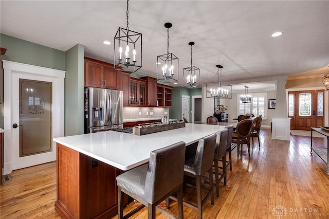 kitchen featuring pendant lighting, stainless steel refrigerator with ice dispenser, light wood finished floors, tasteful backsplash, and glass insert cabinets