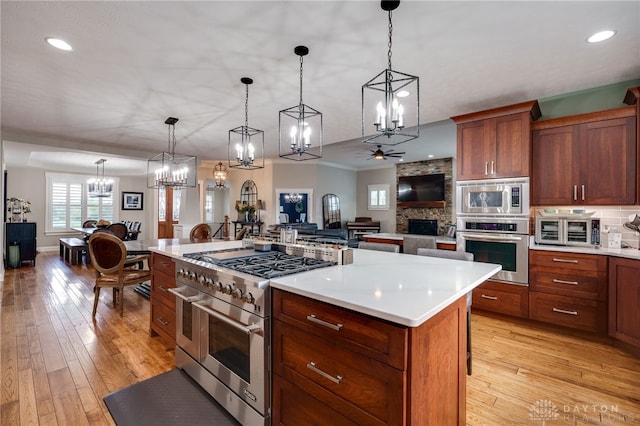 kitchen featuring open floor plan, hanging light fixtures, stainless steel appliances, light countertops, and light wood-type flooring