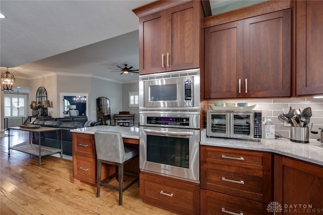 kitchen featuring ceiling fan with notable chandelier, light wood finished floors, stainless steel oven, and crown molding