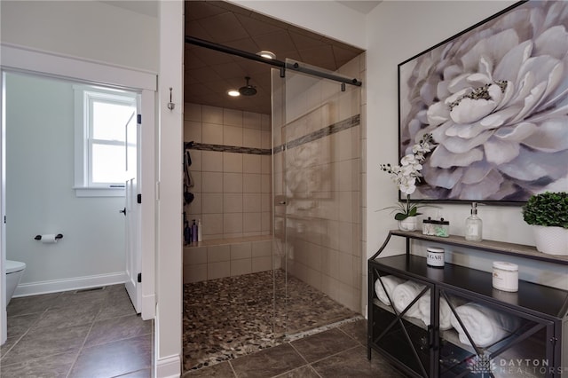 full bath featuring toilet, baseboards, and a tile shower