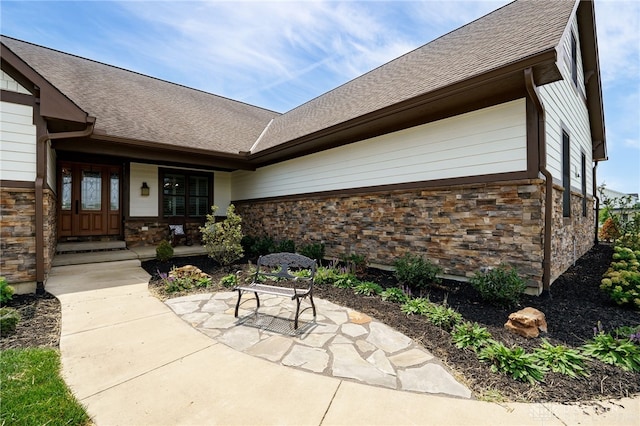 doorway to property with stone siding, a shingled roof, and a patio area