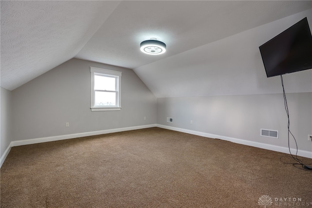 additional living space with lofted ceiling, visible vents, dark carpet, a textured ceiling, and baseboards