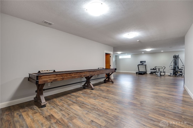 recreation room with baseboards, a textured ceiling, visible vents, and wood finished floors