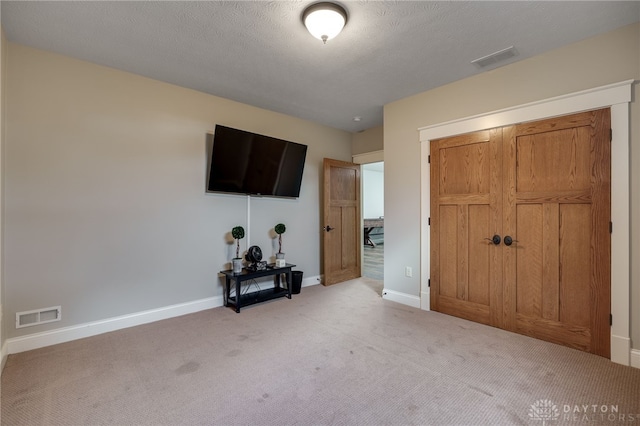 unfurnished bedroom with carpet floors, visible vents, a textured ceiling, and baseboards