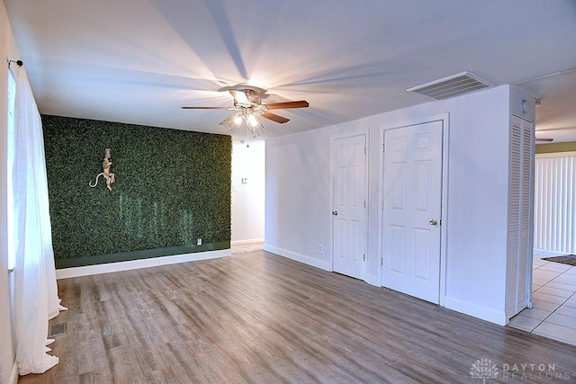 unfurnished bedroom featuring baseboards, an accent wall, visible vents, and wood finished floors