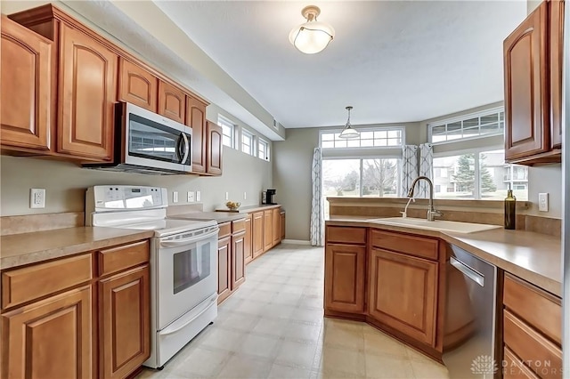 kitchen with brown cabinets, stainless steel appliances, light countertops, hanging light fixtures, and a sink