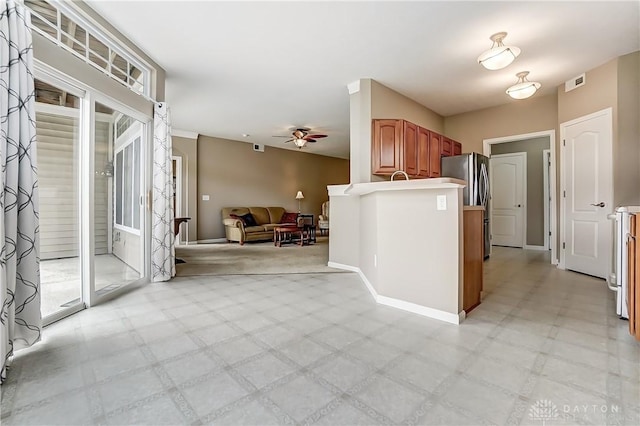 kitchen featuring brown cabinets, light floors, a ceiling fan, open floor plan, and baseboards