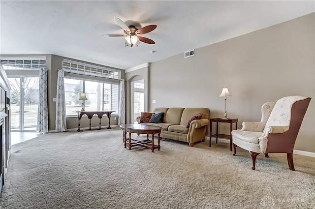 carpeted living area with baseboards, visible vents, arched walkways, and a ceiling fan