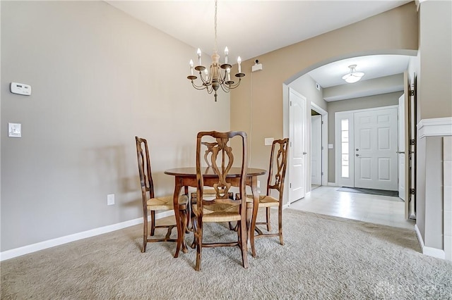 dining area with arched walkways, light colored carpet, a notable chandelier, and baseboards