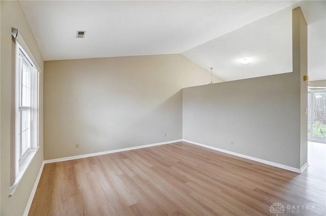 empty room featuring lofted ceiling, light wood-style flooring, a healthy amount of sunlight, and baseboards