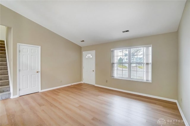 spare room with baseboards, visible vents, light wood-style flooring, stairs, and vaulted ceiling