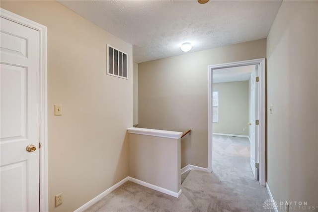 hall featuring an upstairs landing, visible vents, baseboards, and carpet floors