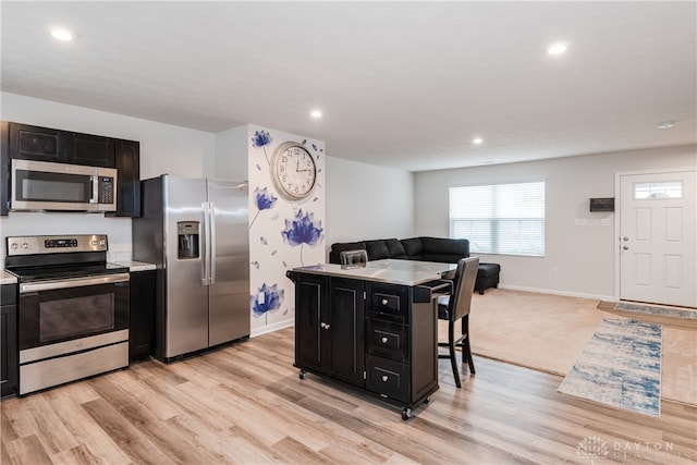 kitchen featuring light countertops, appliances with stainless steel finishes, light wood-style floors, open floor plan, and dark cabinets