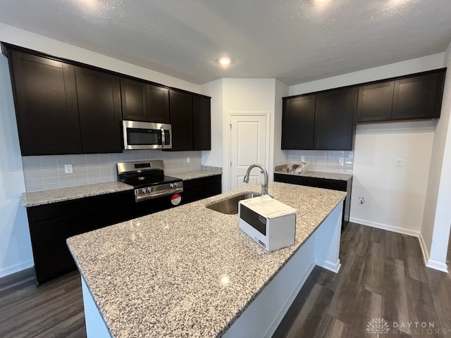 kitchen with stainless steel appliances, a sink, an island with sink, and dark wood-style floors