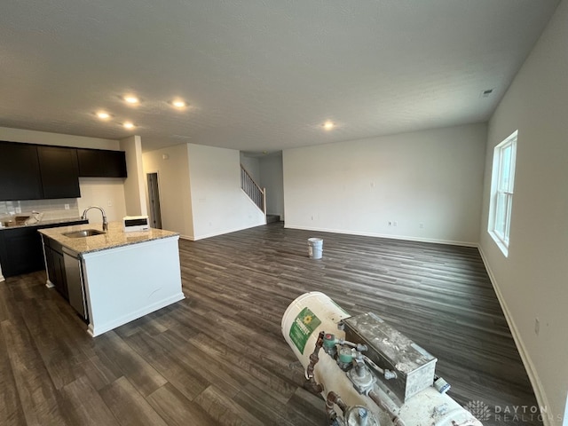 kitchen with a center island with sink, baseboards, open floor plan, dark wood-style flooring, and a sink