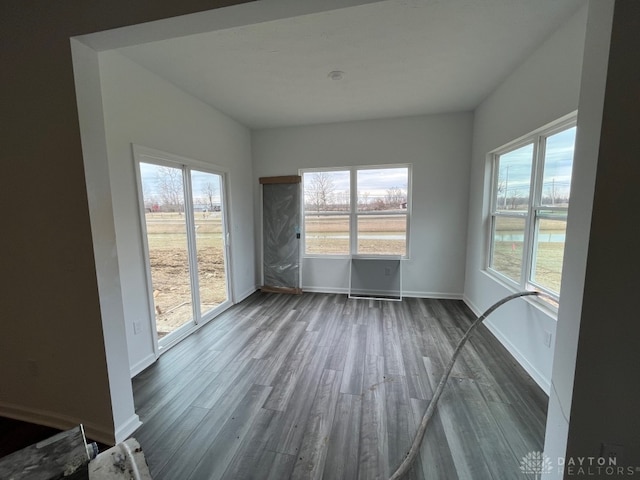 unfurnished room featuring plenty of natural light, baseboards, and dark wood-type flooring