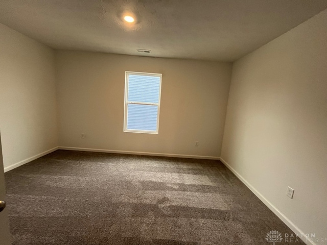 empty room with visible vents, dark carpet, and baseboards