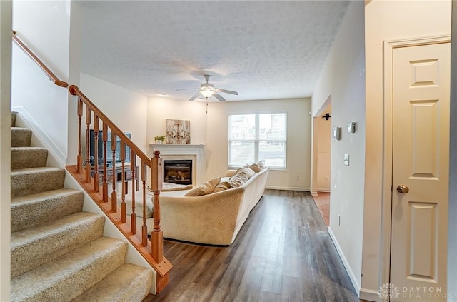 living area with a glass covered fireplace, ceiling fan, stairway, dark wood-type flooring, and a textured ceiling