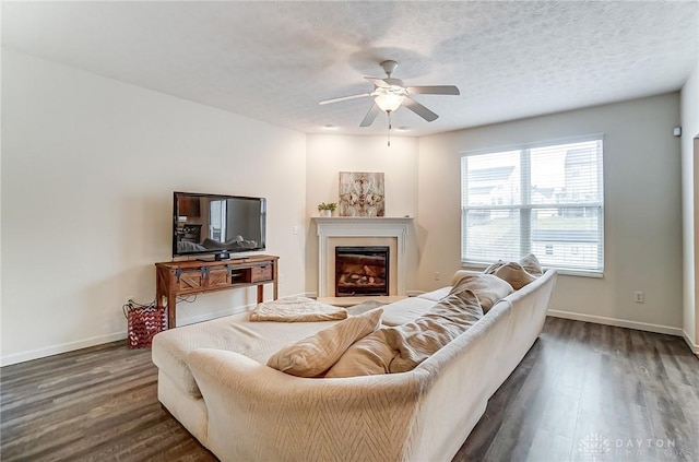 living area with a textured ceiling, dark wood-style flooring, a glass covered fireplace, and baseboards