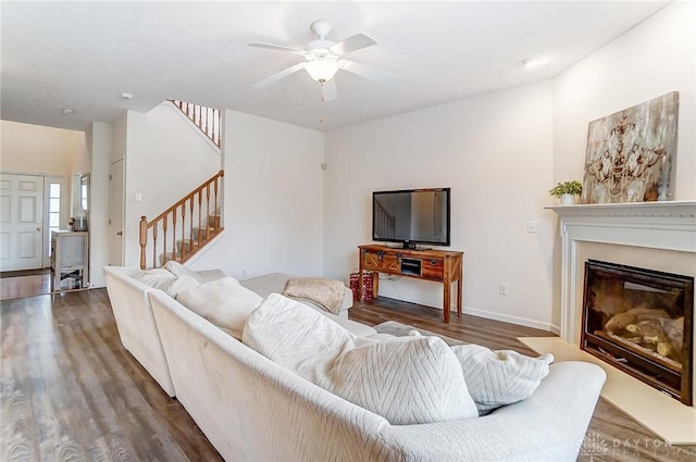 living area featuring ceiling fan, dark wood finished floors, baseboards, stairs, and a glass covered fireplace