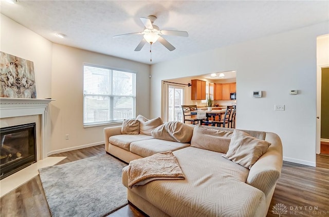 living room with a ceiling fan, a fireplace with flush hearth, baseboards, and wood finished floors