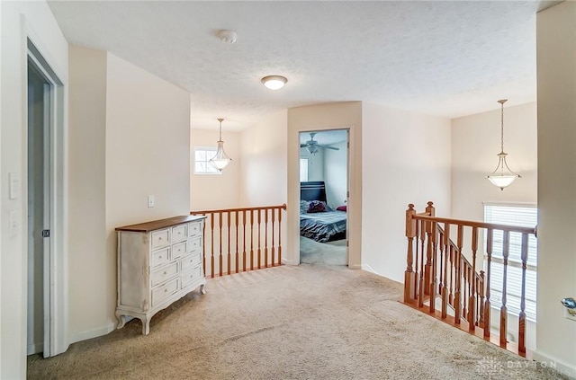 hall featuring a textured ceiling, carpet flooring, and an upstairs landing