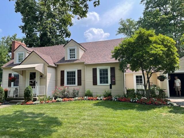 cape cod-style house featuring a shingled roof and a front yard