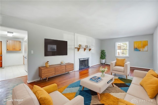 living room featuring light wood finished floors, a fireplace with flush hearth, and baseboards