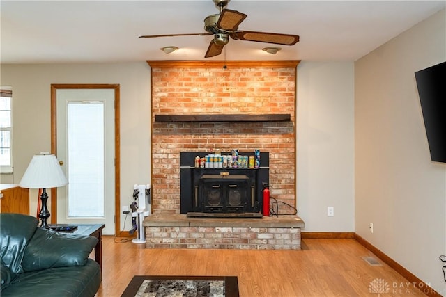 living room featuring wood finished floors, visible vents, a ceiling fan, baseboards, and a wood stove