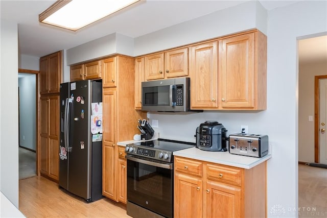 kitchen featuring stainless steel appliances, a toaster, light countertops, and light wood-style floors