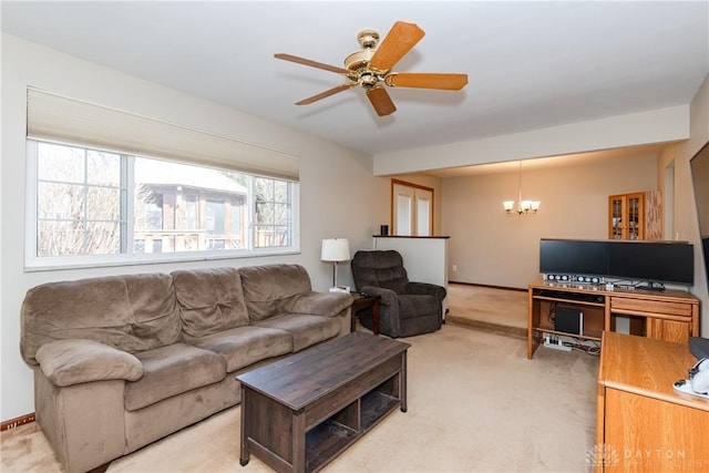 living area featuring light carpet, baseboards, and ceiling fan with notable chandelier