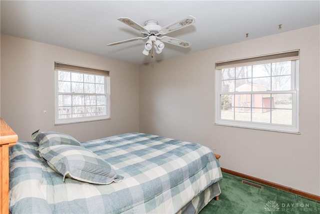 carpeted bedroom featuring visible vents, multiple windows, baseboards, and a ceiling fan