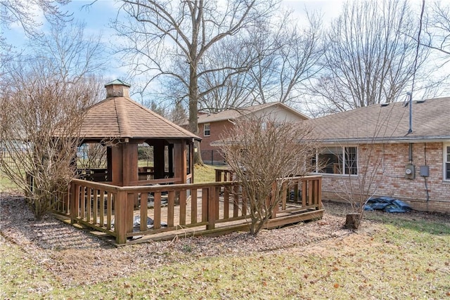 back of house with a shingled roof, a chimney, a deck, a gazebo, and brick siding